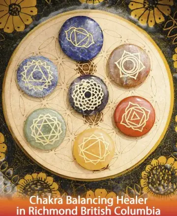 Seven colorful chakra stones with gold symbols are arranged in a circle on a wooden board. The background is dark with a floral pattern. Text reads “Chakra Balancing Healer in Richmond British Columbia.”